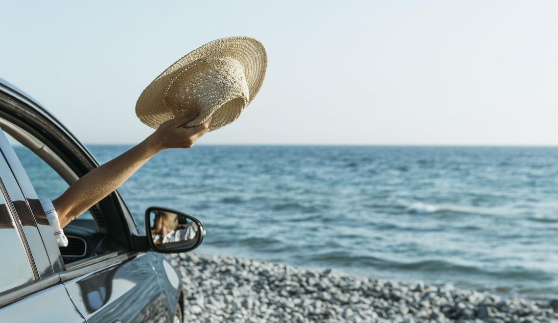 mid-shot-woman-hand-out-car-window-holding-hat-near-sea